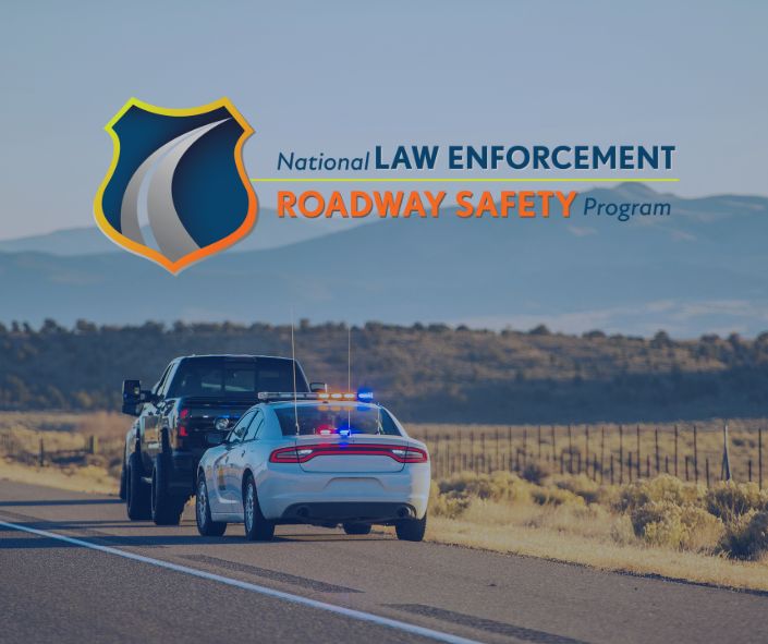 A police vehicle with activated lights stops a truck on a rural road at sunset, with mountains in the background and the 'National Law Enforcement Roadway Safety Program' logo displayed in the corner.